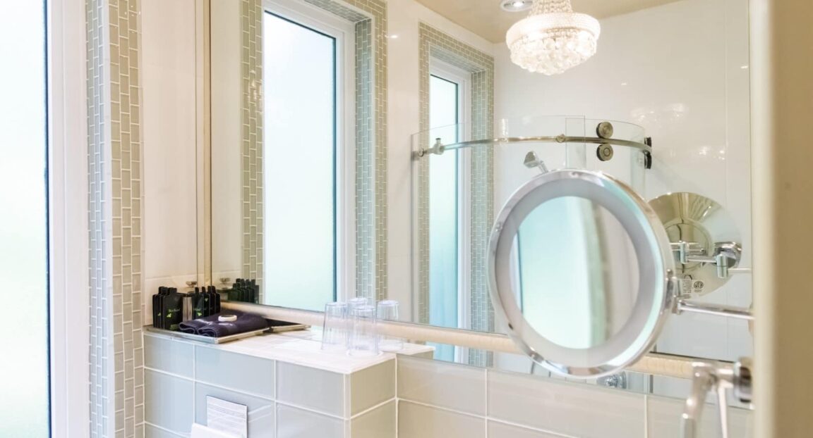 Farnsworth room bathroom mirror with glass walk-in shower and chandelier in the reflection in Stonehurst Place