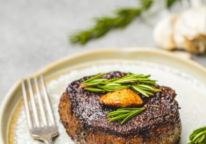 cooked juicy steak with rosemary and garlic garnish on neutral ceramic plate and silver fork